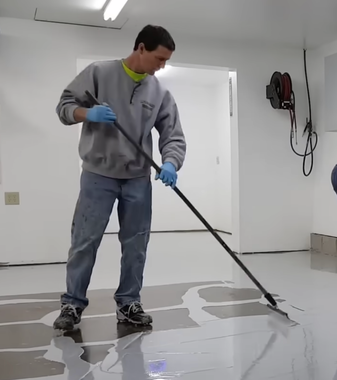 man installing a polyaspartic epoxy floor coating for a garage space over concrete

