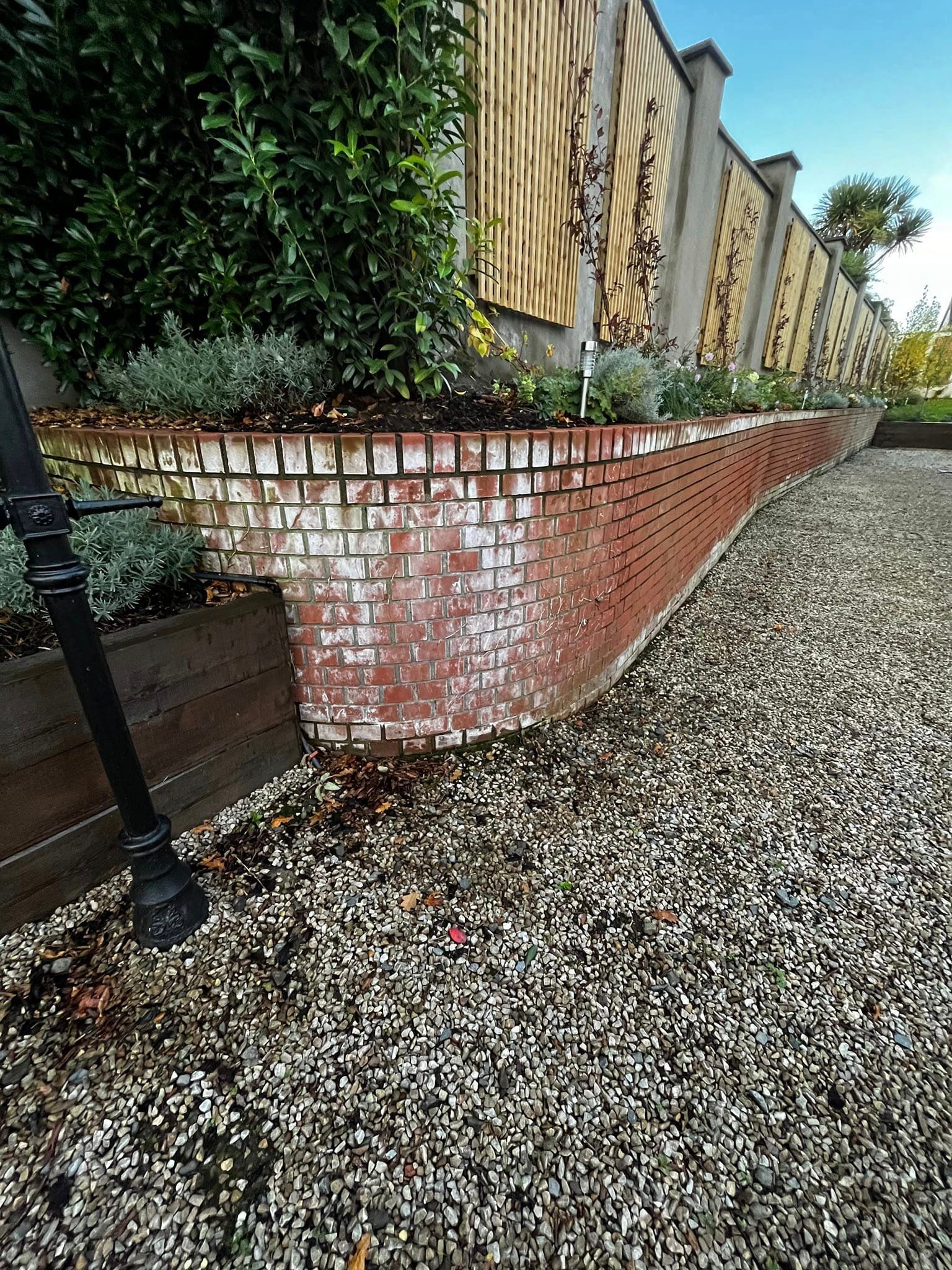 There is a brick wall in the middle of a gravel driveway.