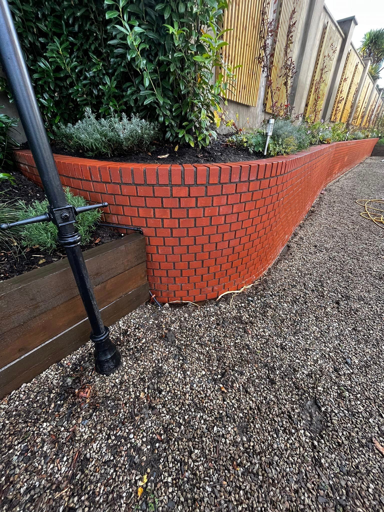 A brick wall surrounds a gravel path in a garden.