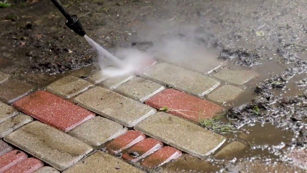 A person is using a high pressure washer to clean a brick walkway.