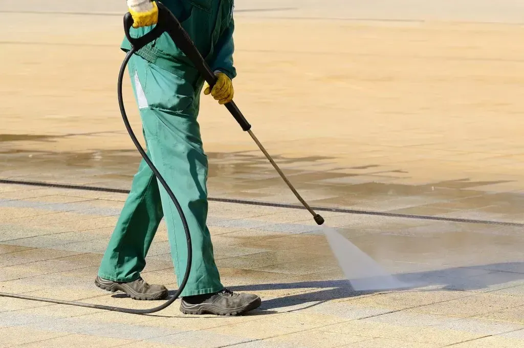 A man in green pants is using a high pressure washer on a concrete surface.