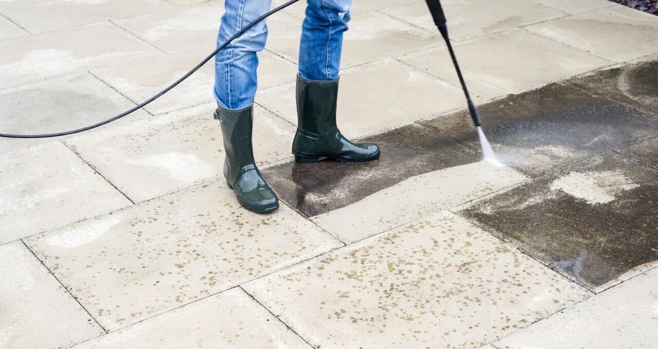 A person is using a high pressure washer to clean a patio.