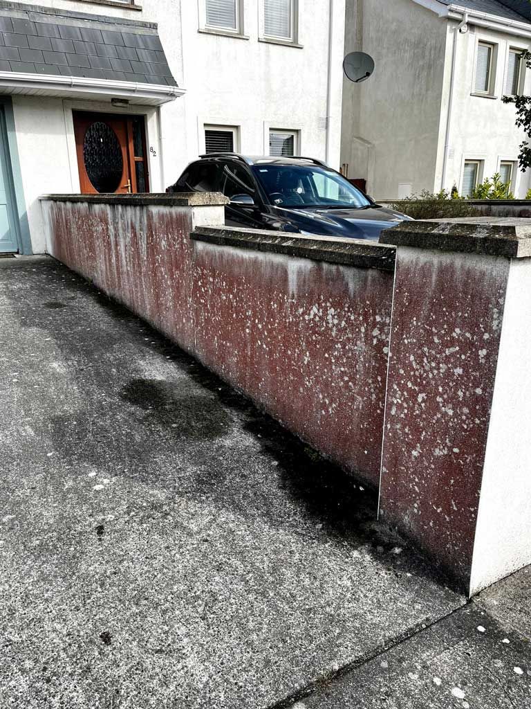 A car is parked in front of a building next to a wall.