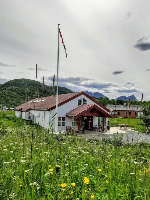 Hvitt hus med rødt tak i en villblomsteng, fjell og overskyet himmel i bakgrunnen