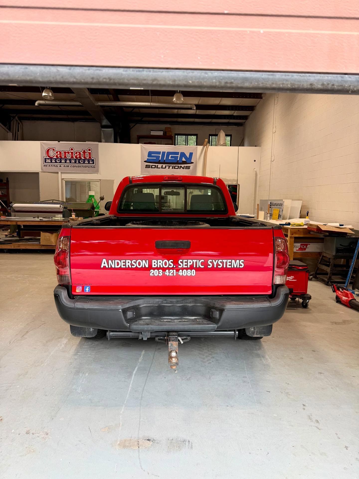 Red pickup truck parked inside a garage with business logos in the background.