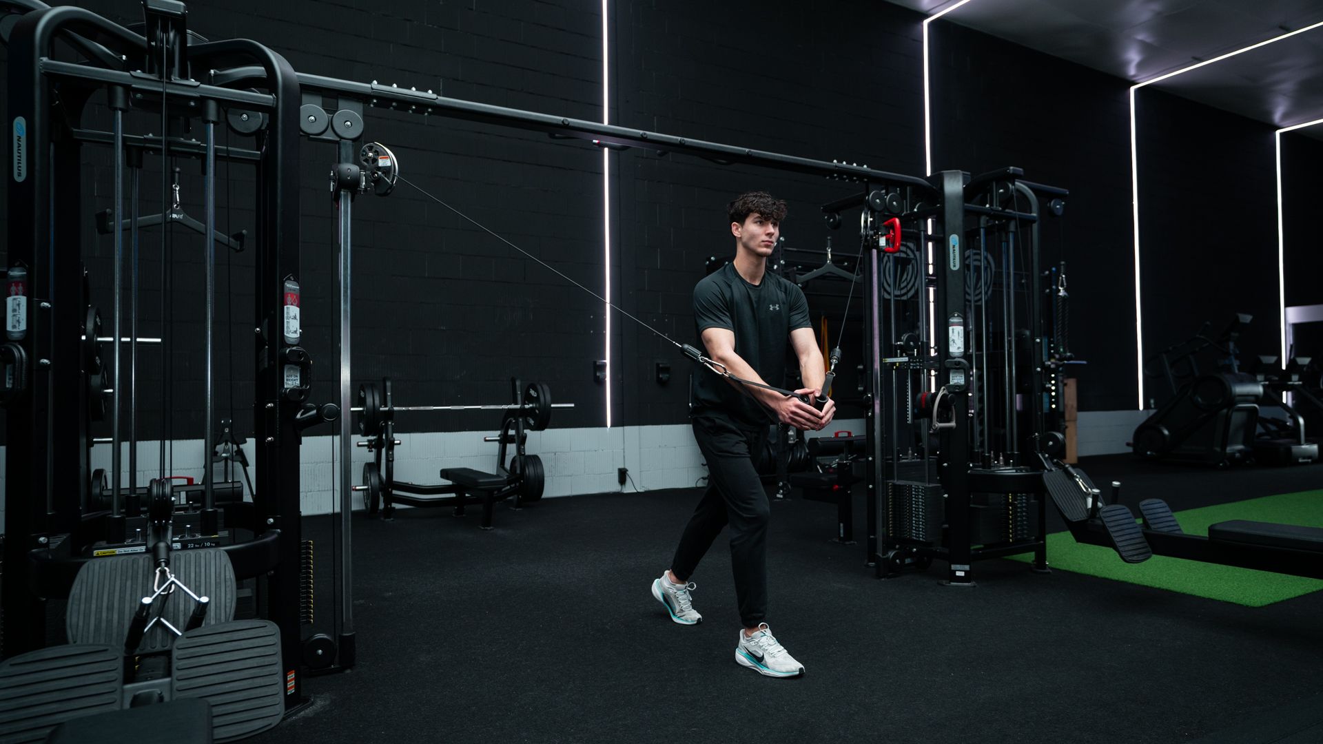 Twee mensen tillen halters in een sportschool, waarbij een van hen een gewicht boven zijn hoofd tilt naast een spiegel.