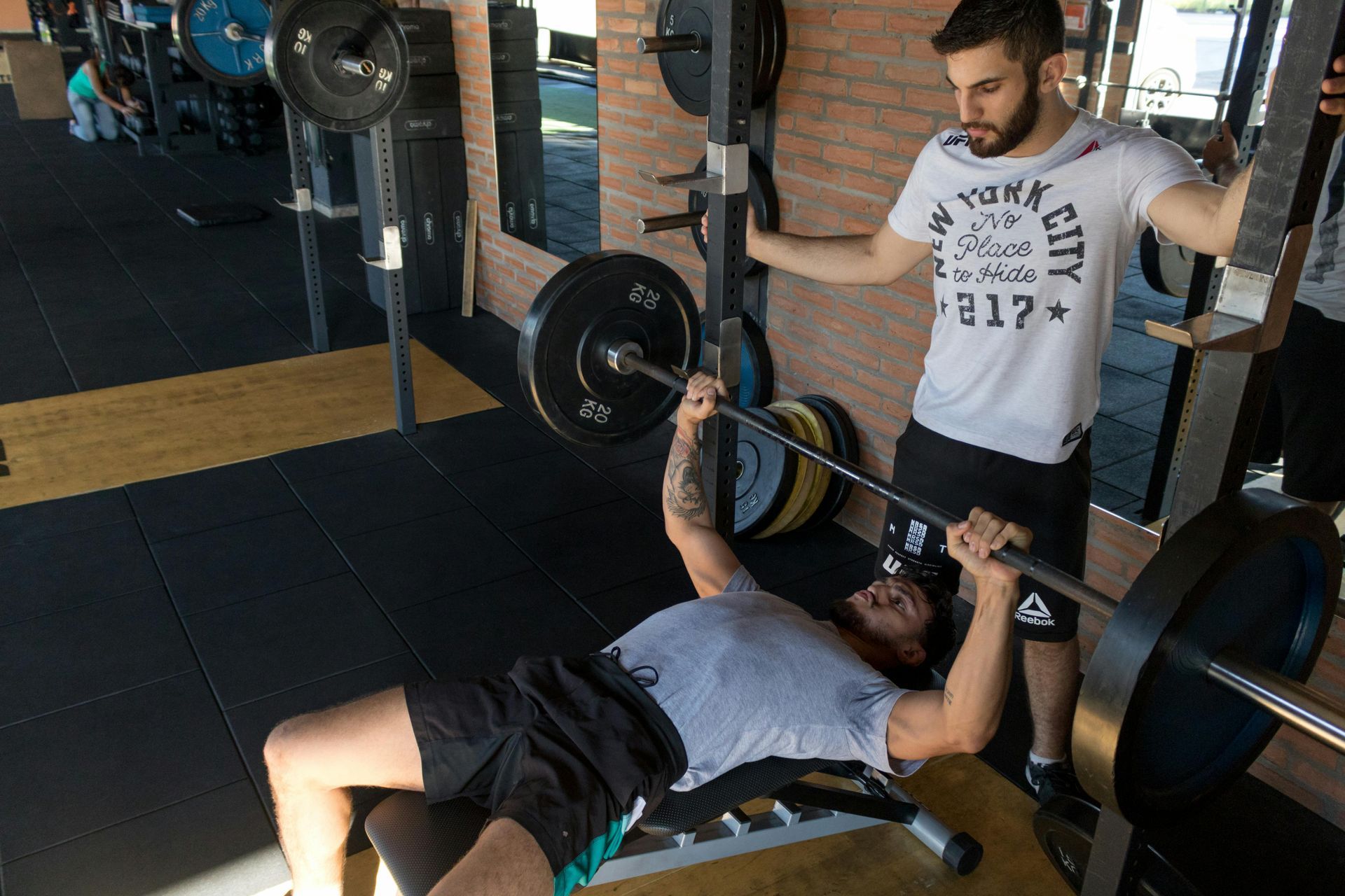 Een man tilt een halterstang op terwijl een trainer hem in de gaten houdt in een sportschool.