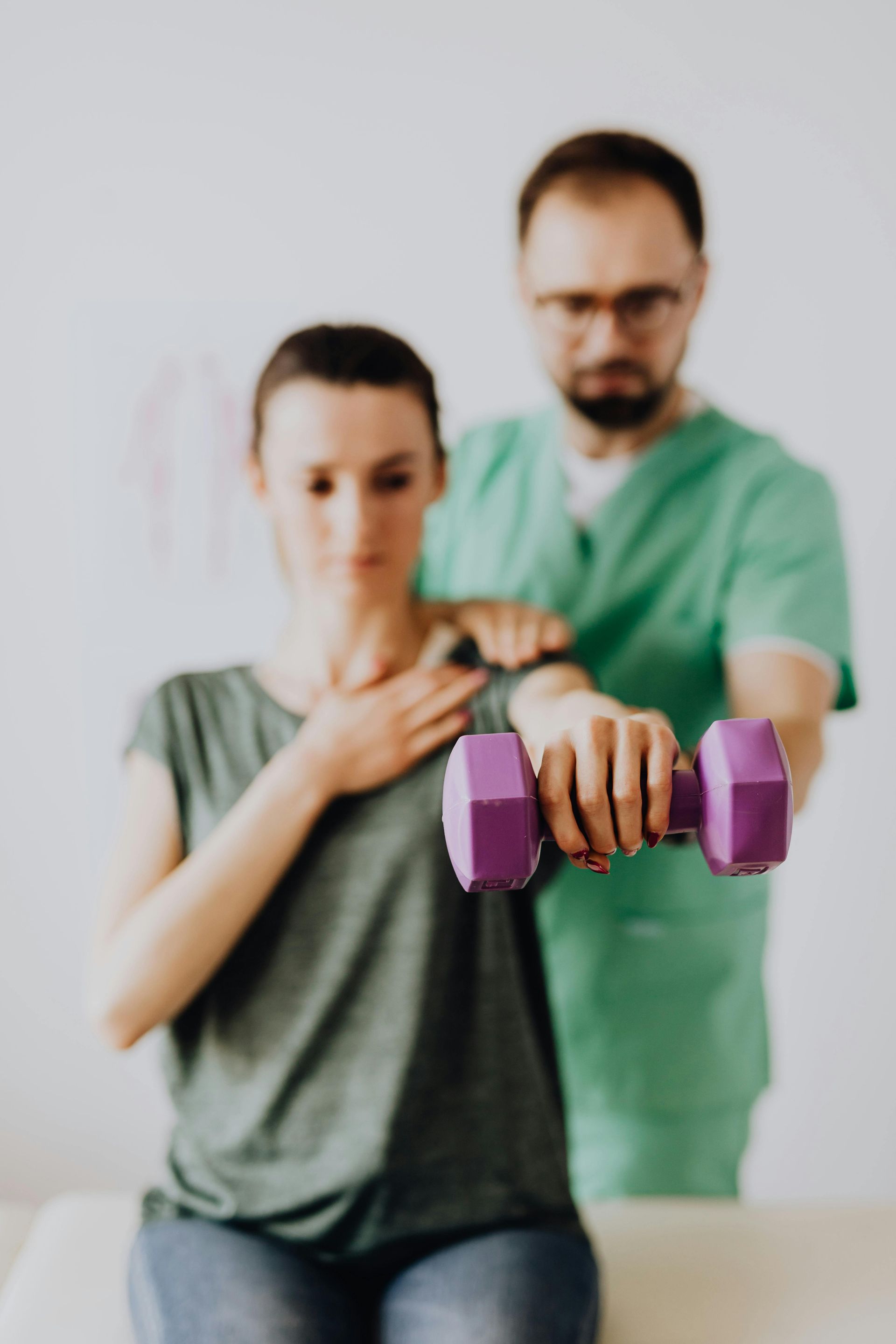 Twee mensen doen binnen oefeningen met paarse dumbbells, één staat vooraan en de ander staat erachter om te helpen.