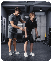 Een trainer helpt een cliënt met een deadlift in een sportschool; beiden dragen sportkleding.