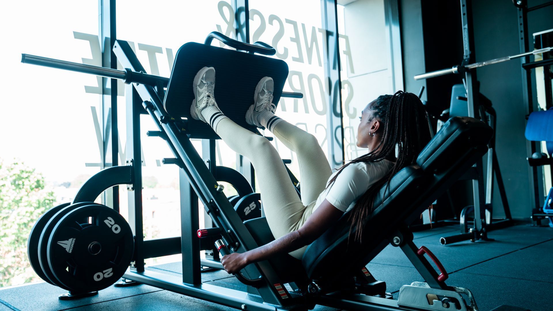 Een persoon die oefeningen doet op een legpress-apparaat in een sportschool met grote ramen.