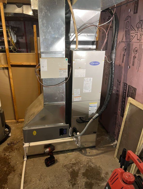 Un climatiseur en acier inoxydable se trouve dans un sous-sol à côté d'un aspirateur.