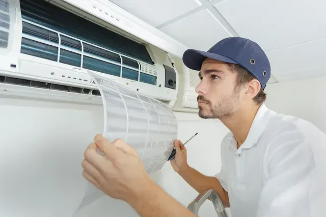 Un homme portant une casquette inspecte le filtre d'un climatiseur.