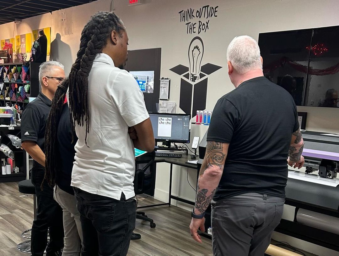 Four people look at a computer screen in a print shop.