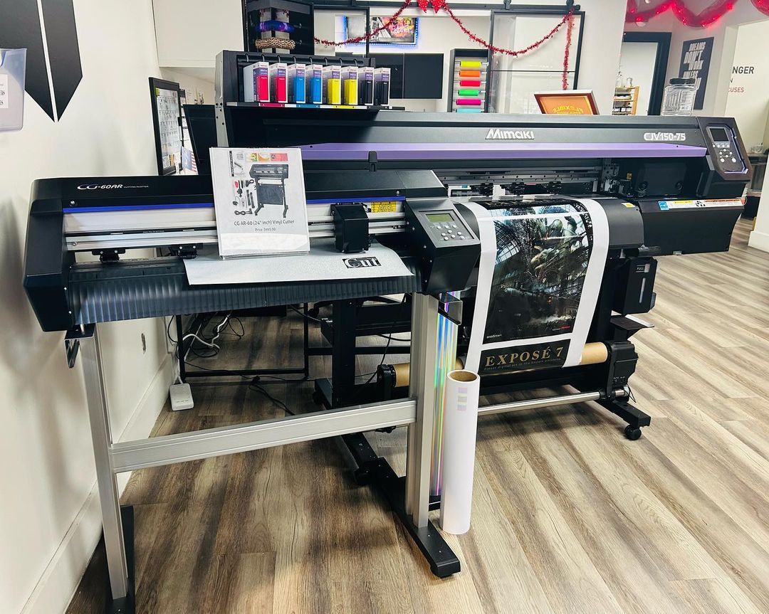 Large format printer printing a black and white image, ink cartridges displayed above.