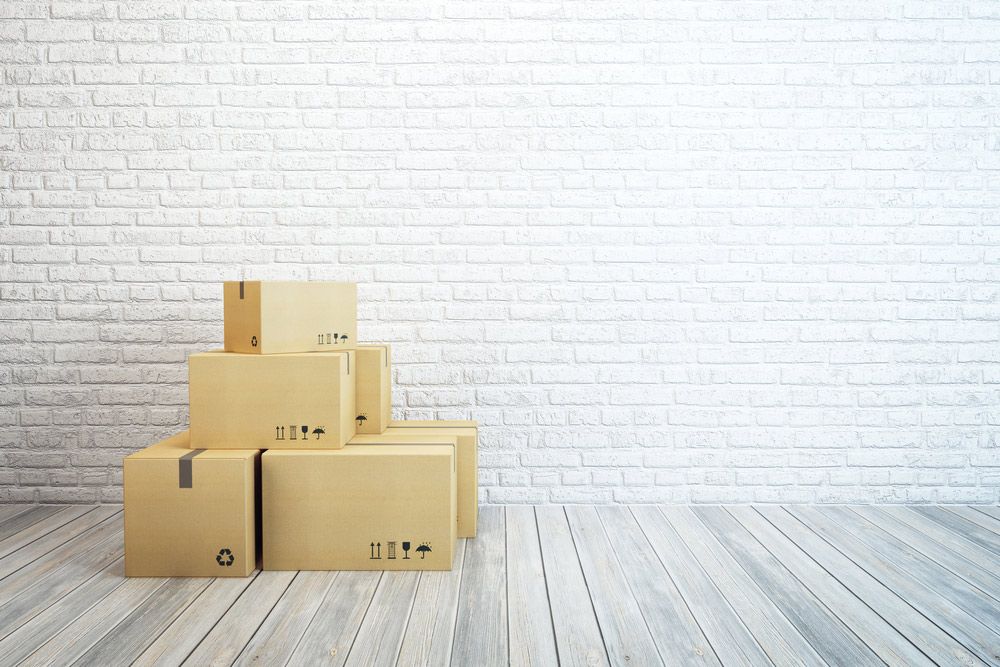 A Stack Of Cardboard Boxes Sitting On A Wooden Floor In Front Of A White Brick Wall  — Dawson Moving & Storage NQ in Brisbane, QLD