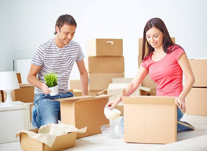 A Man And A Woman Are Sitting On The Floor Packing Boxes — Dawson Moving & Storage NQ in Mount St John, QLD
