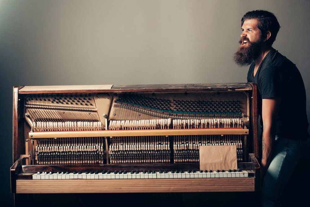 A Man With A Beard Is Standing Next To A Piano — Dawson Moving & Storage NQ in Mount St John, QLD