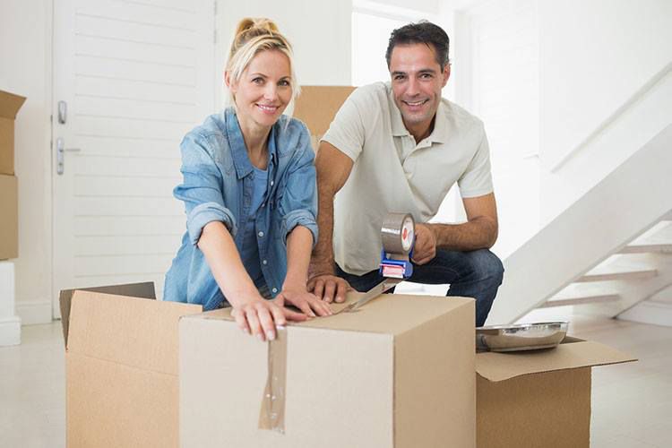 A Man And A Woman Are Sitting On Cardboard Boxes In A New Home — Dawson Moving & Storage NQ in Mount St John, QLD