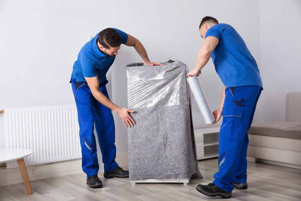 Two Men Are Wrapping A Refrigerator With Plastic Wrap In A Living Room — Dawson Moving & Storage NQ in Mackay, QLD