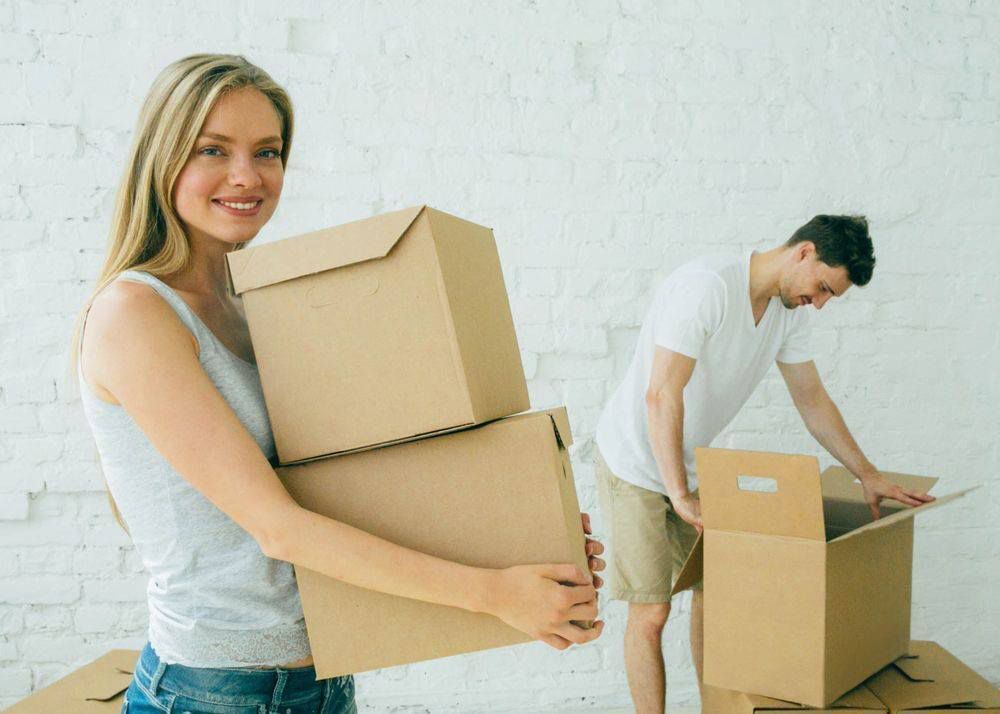 A Woman Is Holding A Stack Of Cardboard Boxes While A Man Is Opening A Box — Dawson Moving & Storage NQ in Mount St John, QLD