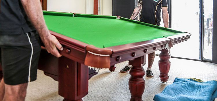 A Man Is Carrying A Pool Table In A Room — Dawson Moving & Storage NQ in Mount St John, QLD