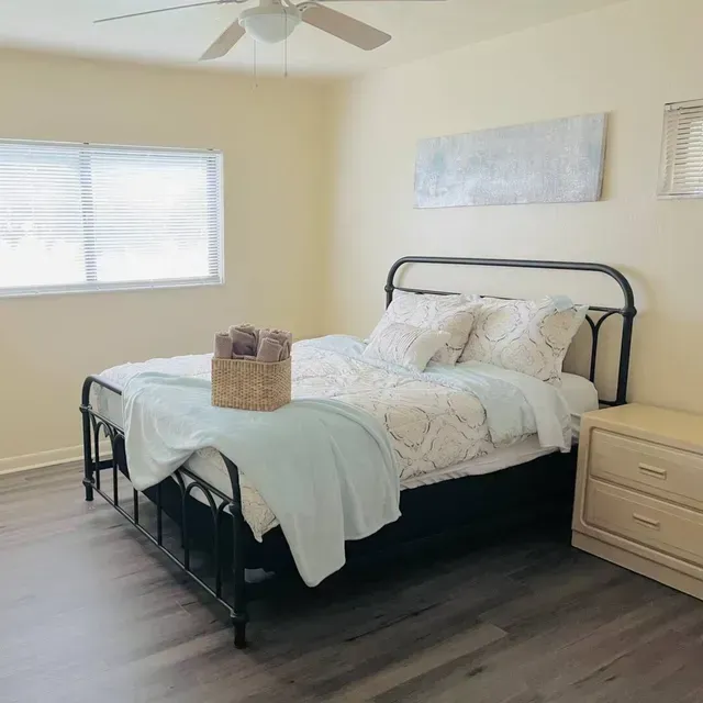 Bedroom with bed, nightstand, window, and abstract art; light walls, dark floor.