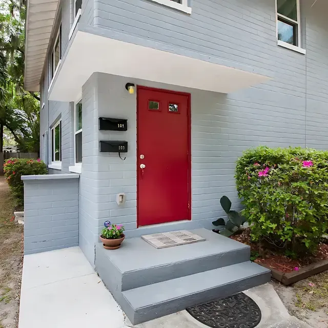 Gray house with red door, concrete steps, and mailbox.