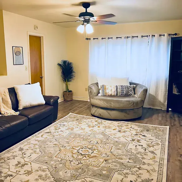 Living room with brown leather sofa, tan swivel chair, and large patterned rug.