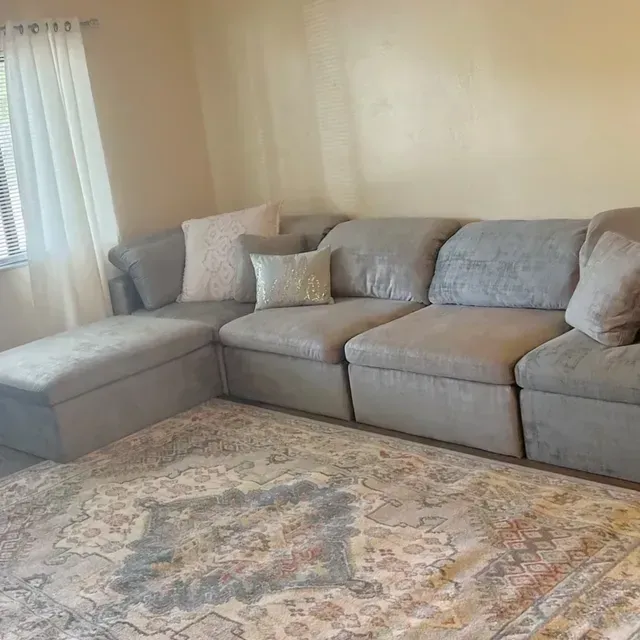 Gray sectional sofa with pillows on a patterned rug in a room with a window.