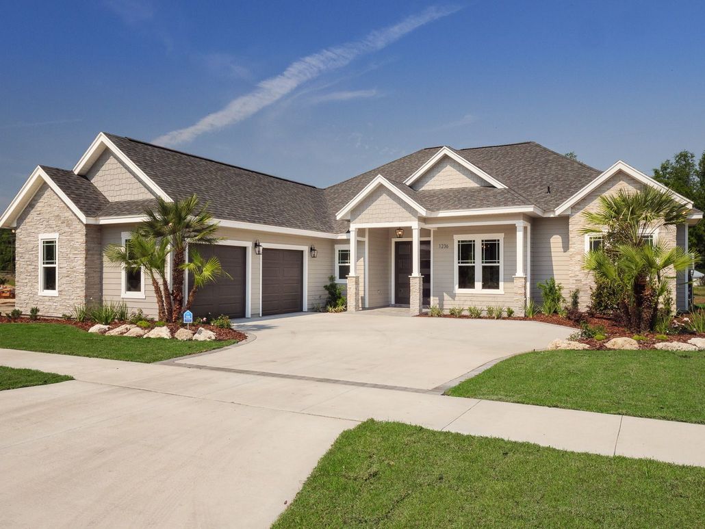 Light gray suburban home with two-car garage, manicured lawn, and driveway on a sunny day.