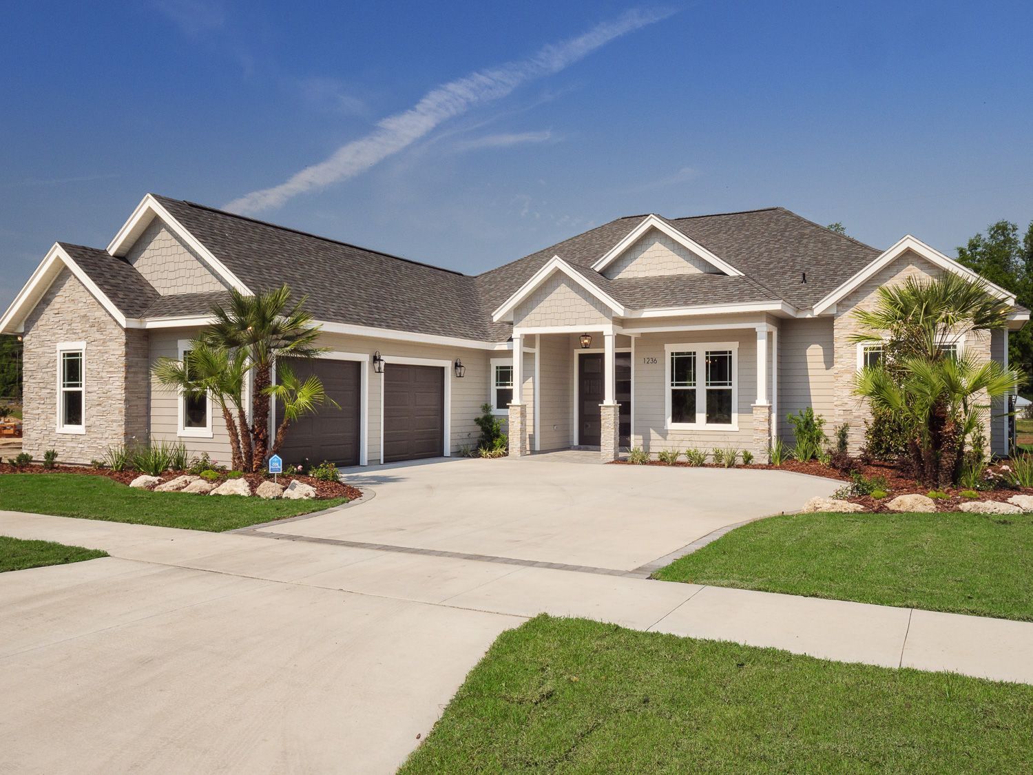 Light gray suburban home with two-car garage, manicured lawn, and driveway on a sunny day.