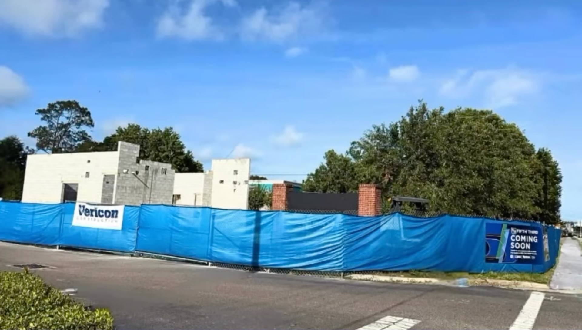Construction site fenced with blue tarp; building partially erected under a blue sky.