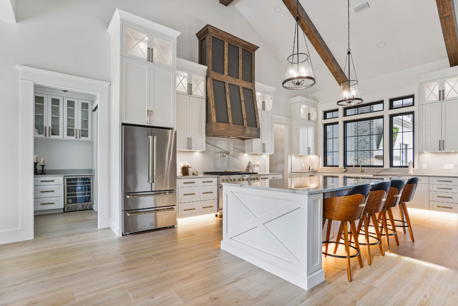Spacious white kitchen with island, stainless steel refrigerator, and wooden beams.