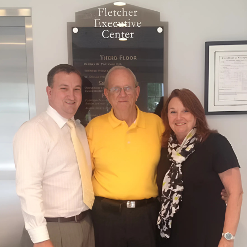 Three people pose in front of a sign at the Fletcher Executive Center. Two men and a woman smile.