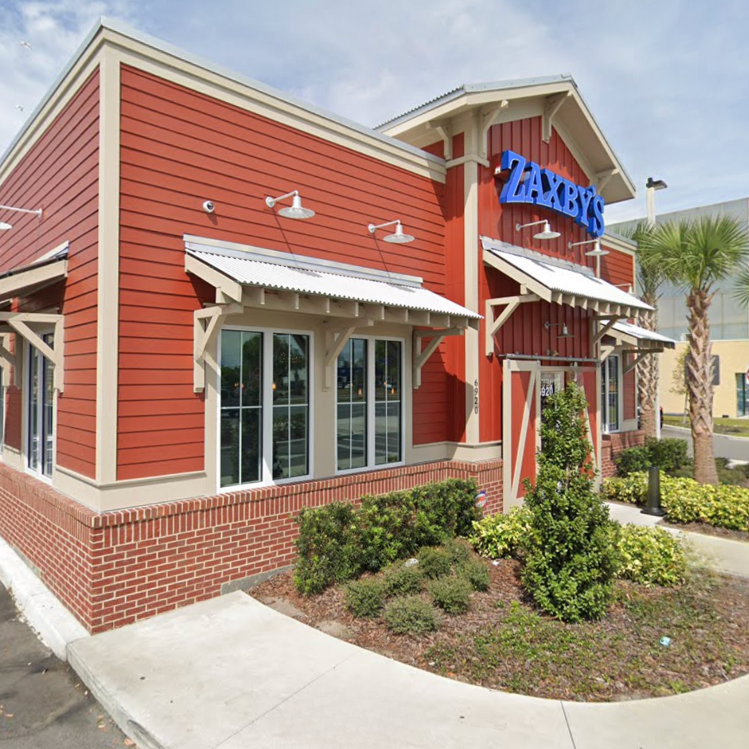 Zaxby's restaurant with red siding, awnings, and a sign. Palm trees nearby.