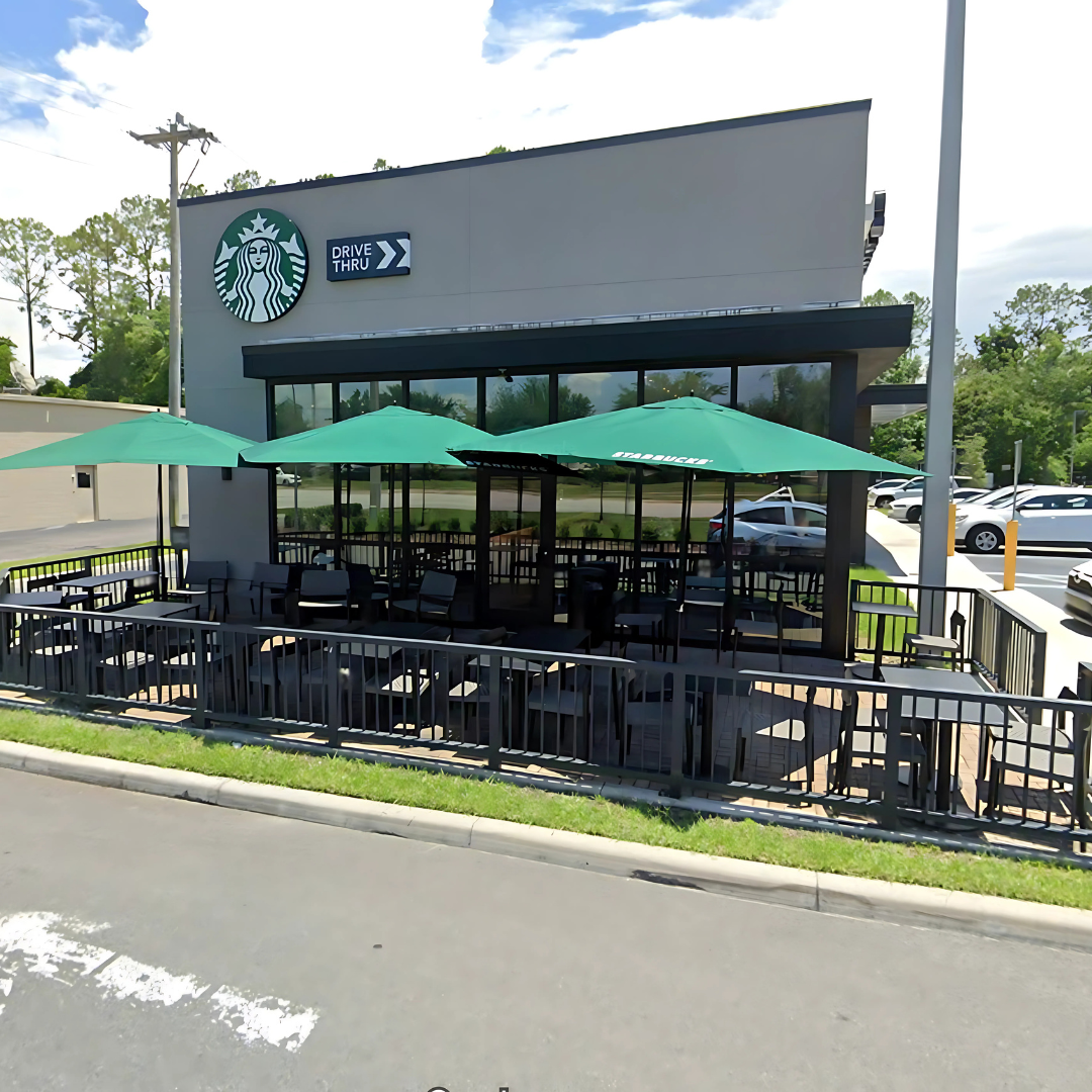 Exterior of Starbucks with green umbrellas, outdoor seating, and large windows.