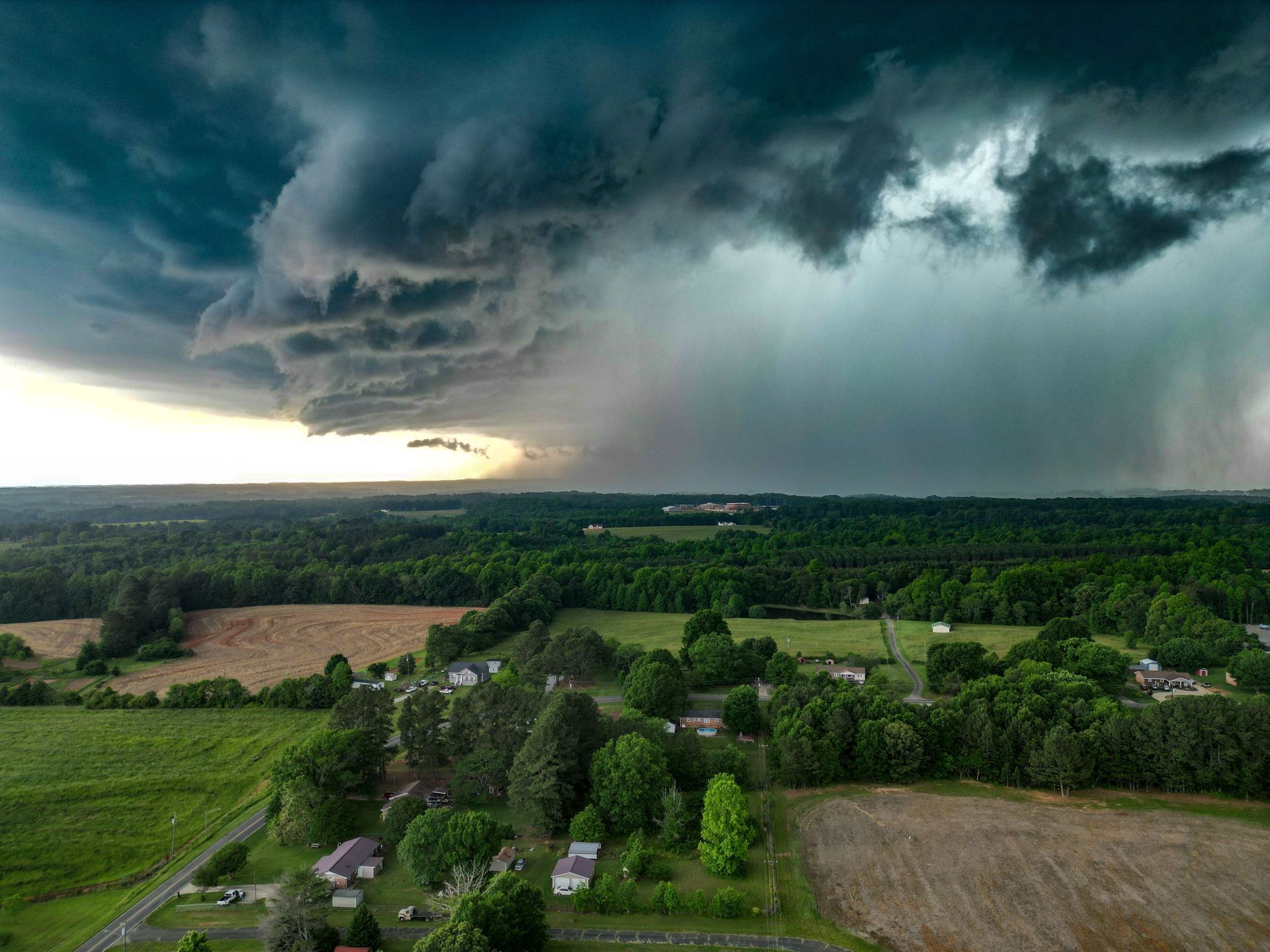 Dark storm clouds over a rural landscape with green fields and a distant rain shaft