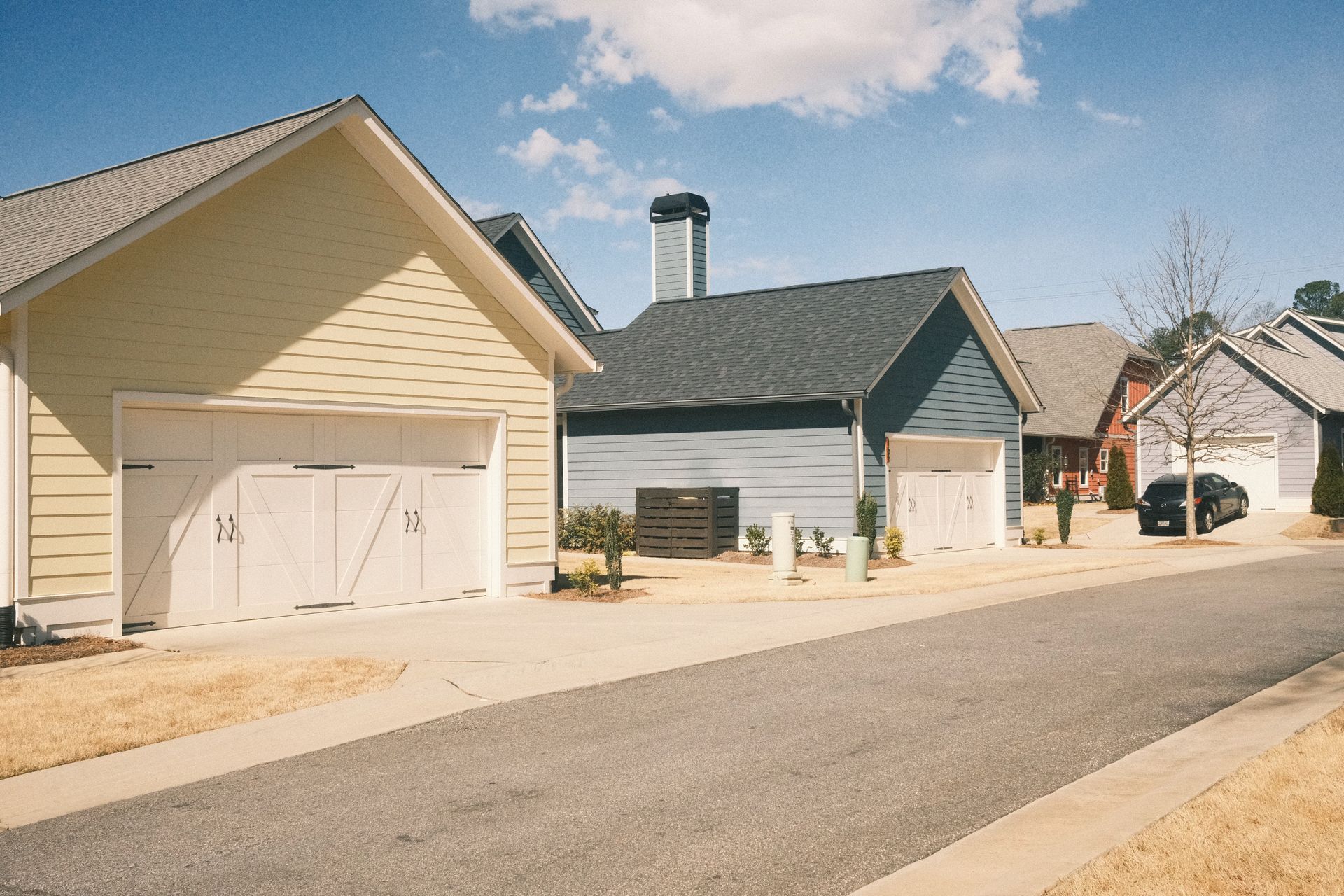Suburban street with beige and gray houses, garages, and a paved road under a blue sky