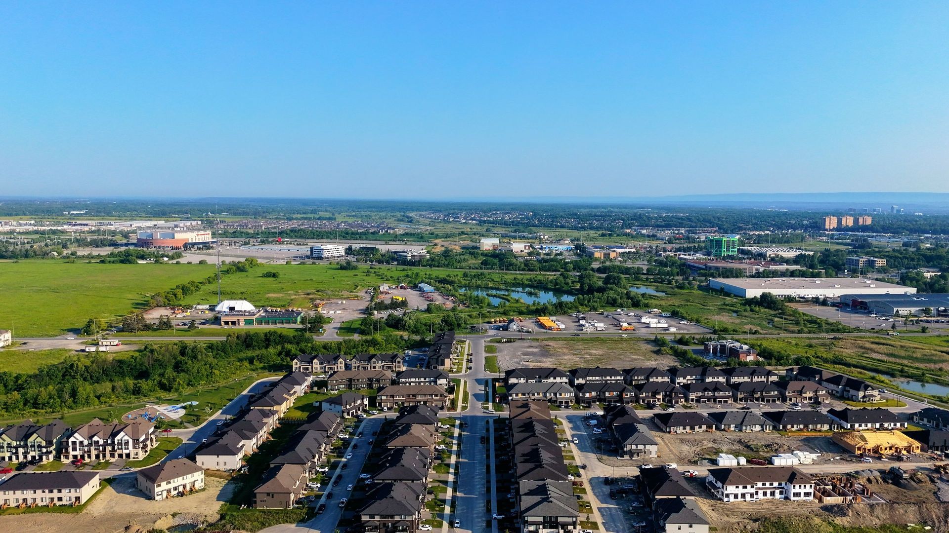 Aerial view of a suburban neighborhood with green fields, roads, and buildings under a clear blue sky