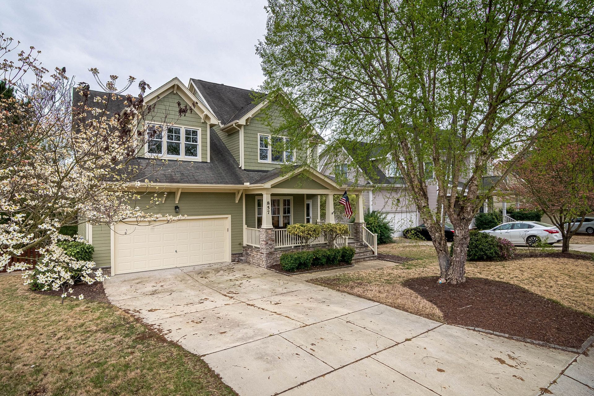 Two-story suburban house with beige siding, a two-car garage, and a tree-lined driveway