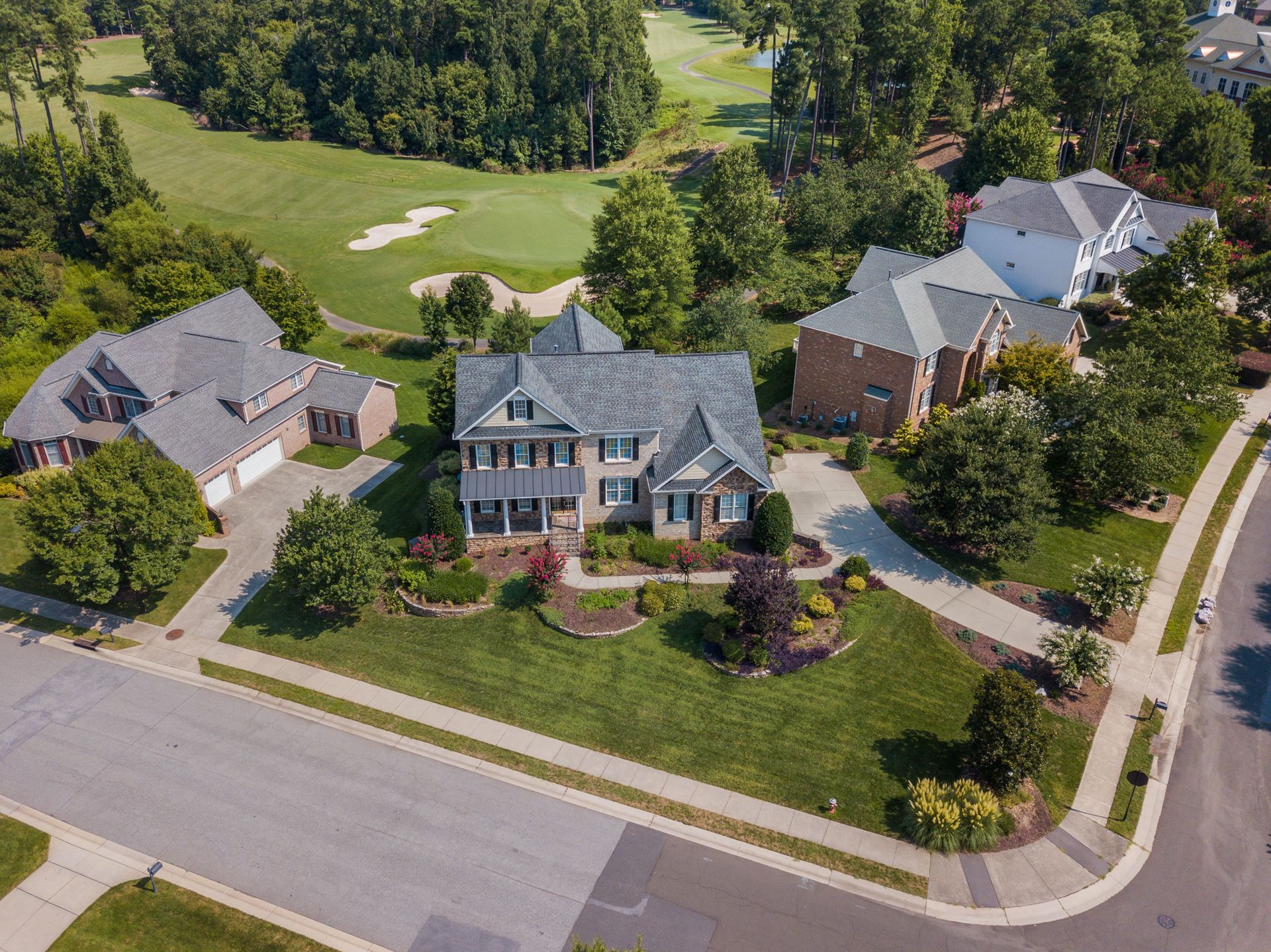 Aerial view of three suburban houses on a curved street beside a green golf course