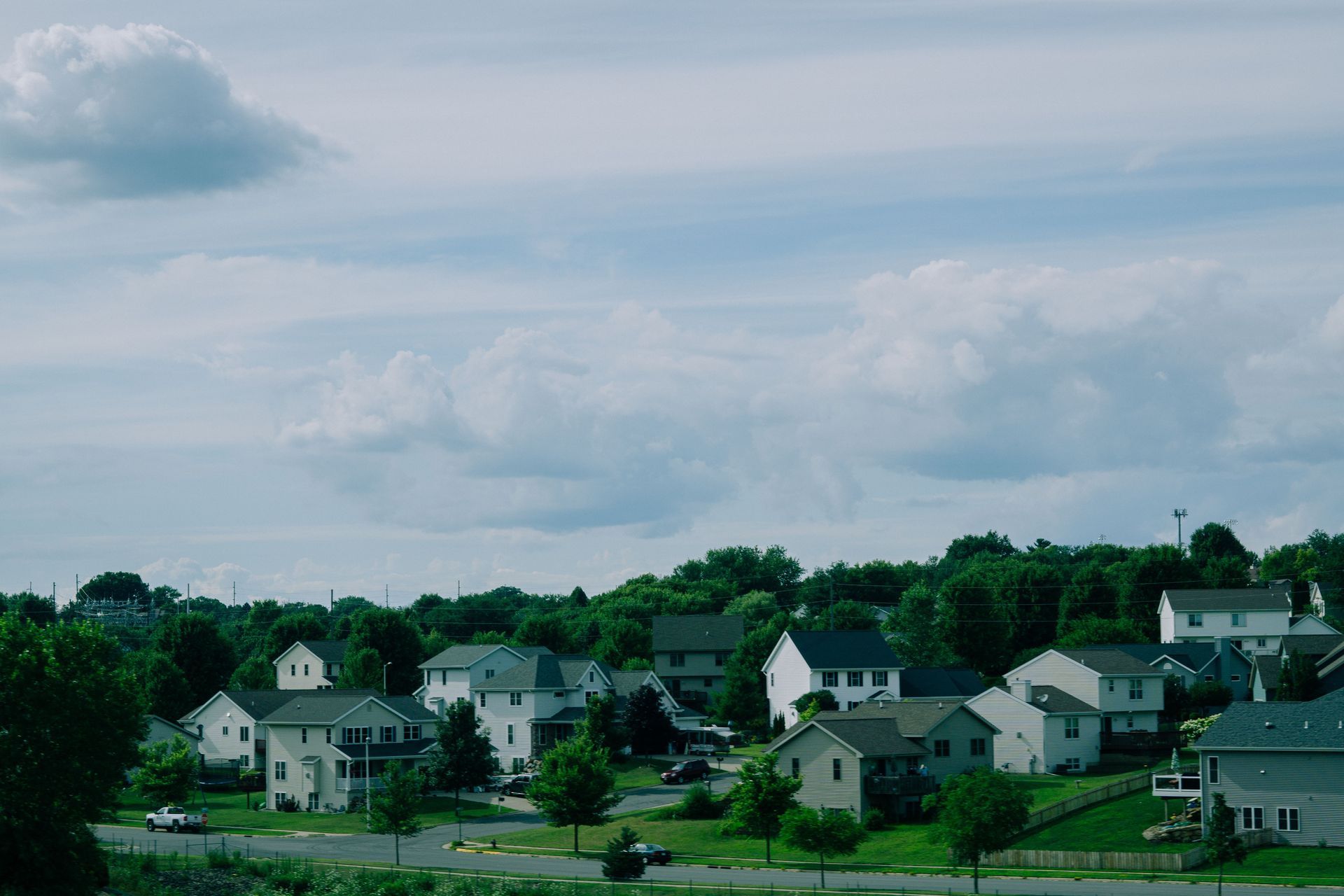Wide aerial view of a suburban neighborhood with green fields and a clear blue sky