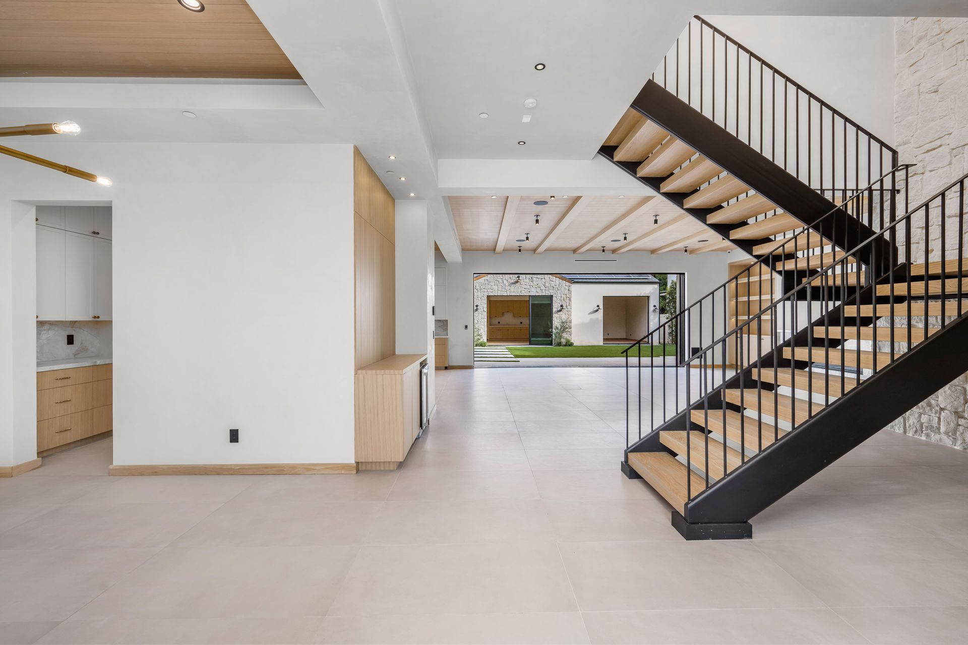 Modern open-plan interior with a staircase, white walls, and wood-accented ceiling.