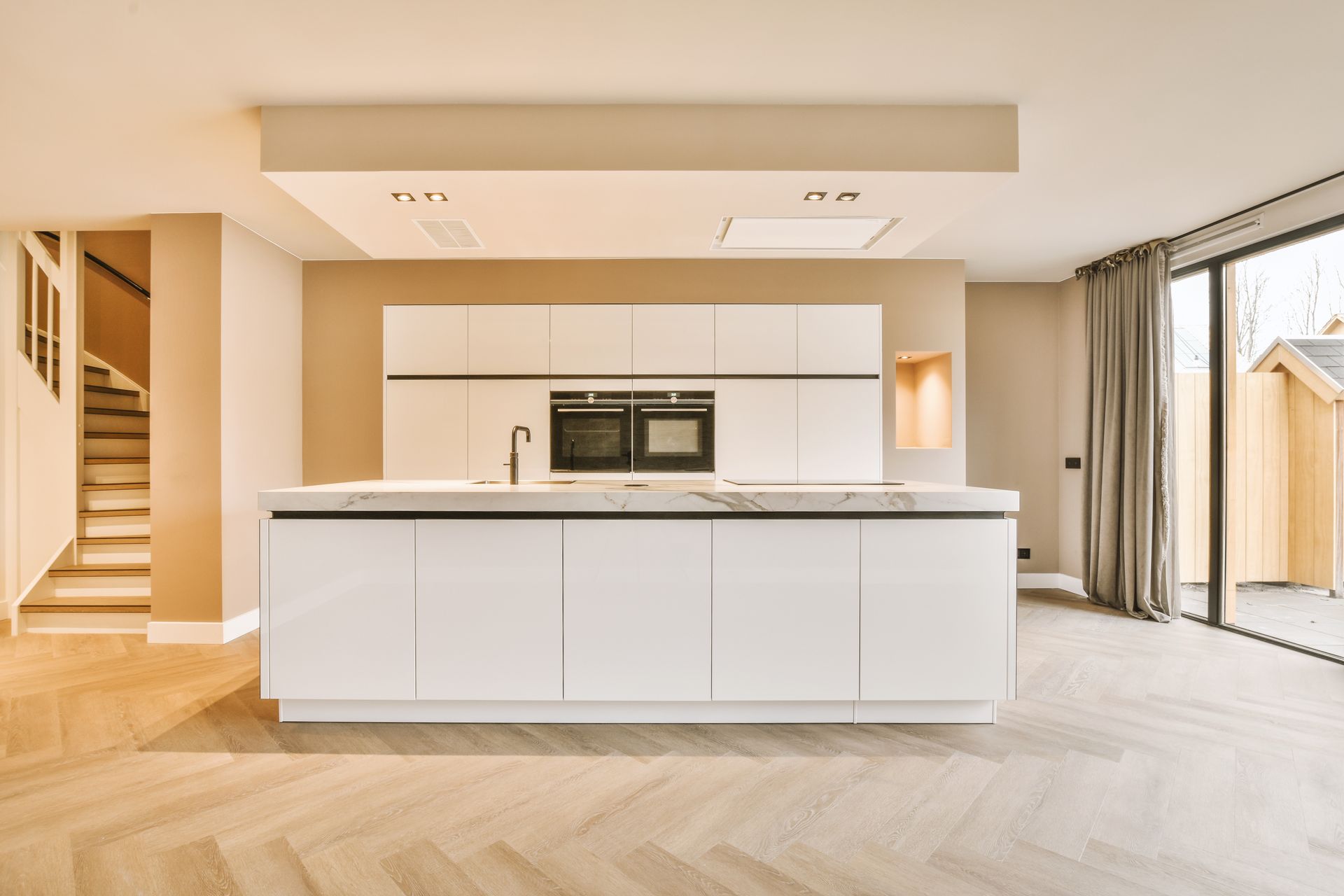 Bright modern kitchen with white island, built-in oven, wood floors, and large windows with curtains