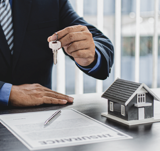 Hand holding house keys over signed real estate documents with a model house on the desk