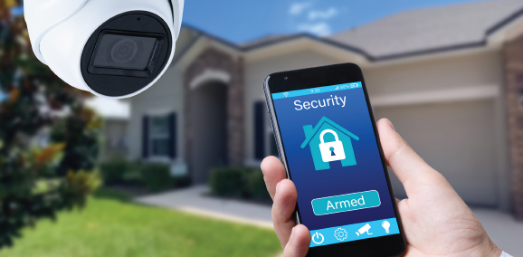 Hand holding a smartphone security app, with a home surveillance camera and house in the background