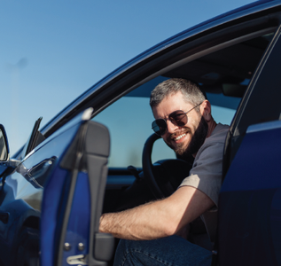 Smiling man in sunglasses leaning out of a blue car with the driver’s door open