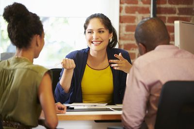 A woman is sitting at a table talking to two people.