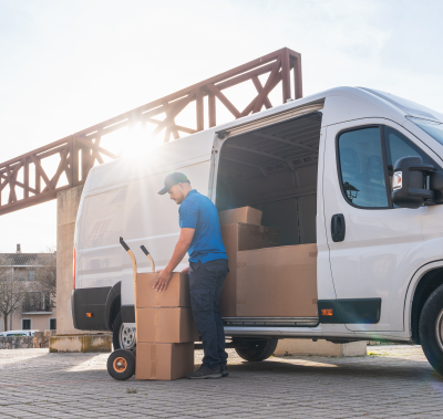 Delivery worker loading cardboard boxes from a van in a sunny warehouse yard