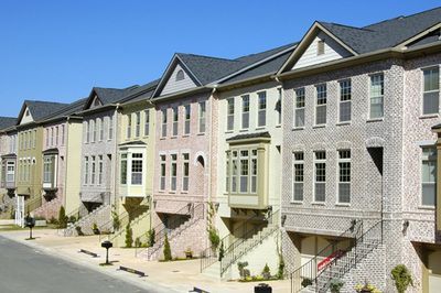 Row of pastel townhouses on a sunny street with stone facades and small front steps
